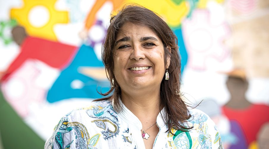 A woman smiles and stands in front of a colorful neighborhood mural.