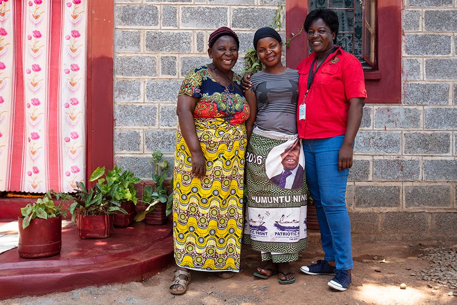 Lucy stands outside her home with two other women.