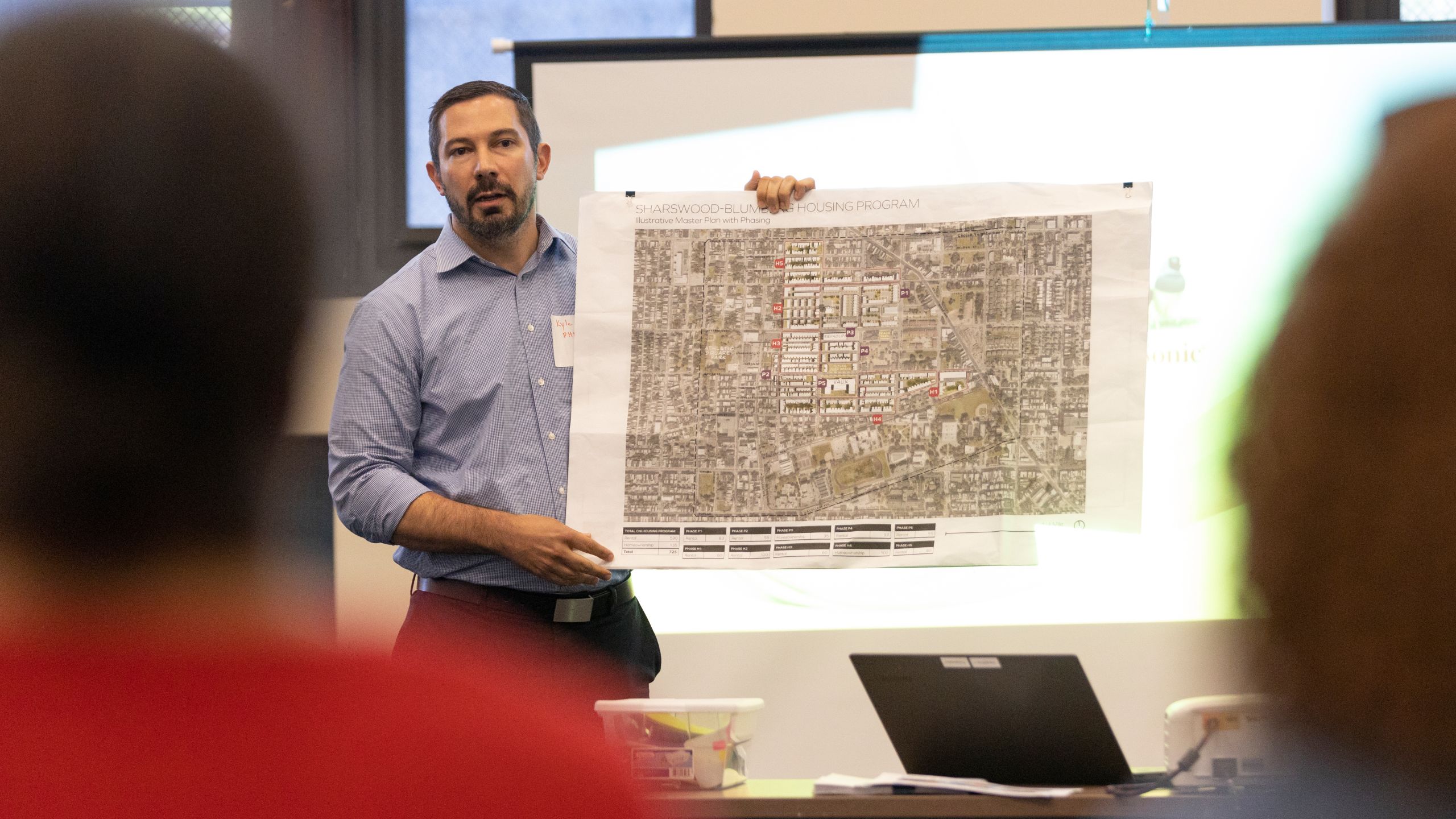 A man presents a large print of a neighborhood plan as residents look on.
