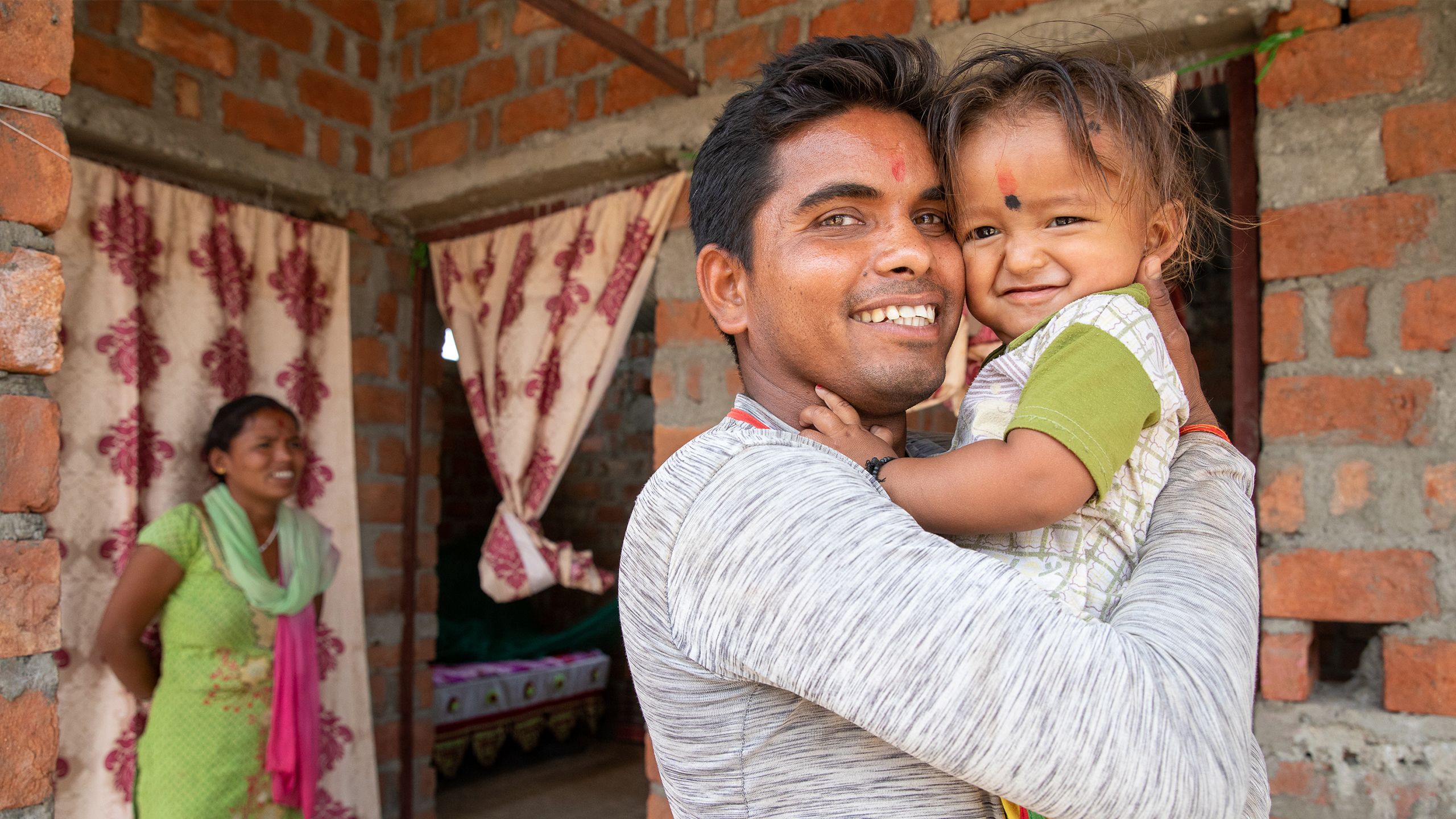 Bir Ram hugs his small child in the doorway of their home.