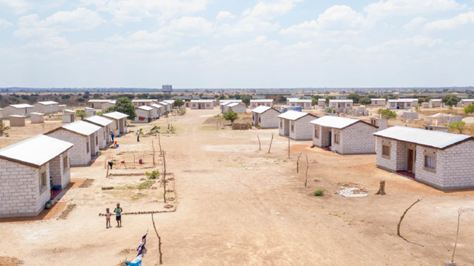 Small brick white homes with two windows each and a door in the middle lined up across from each other on a wide dirt avenue.