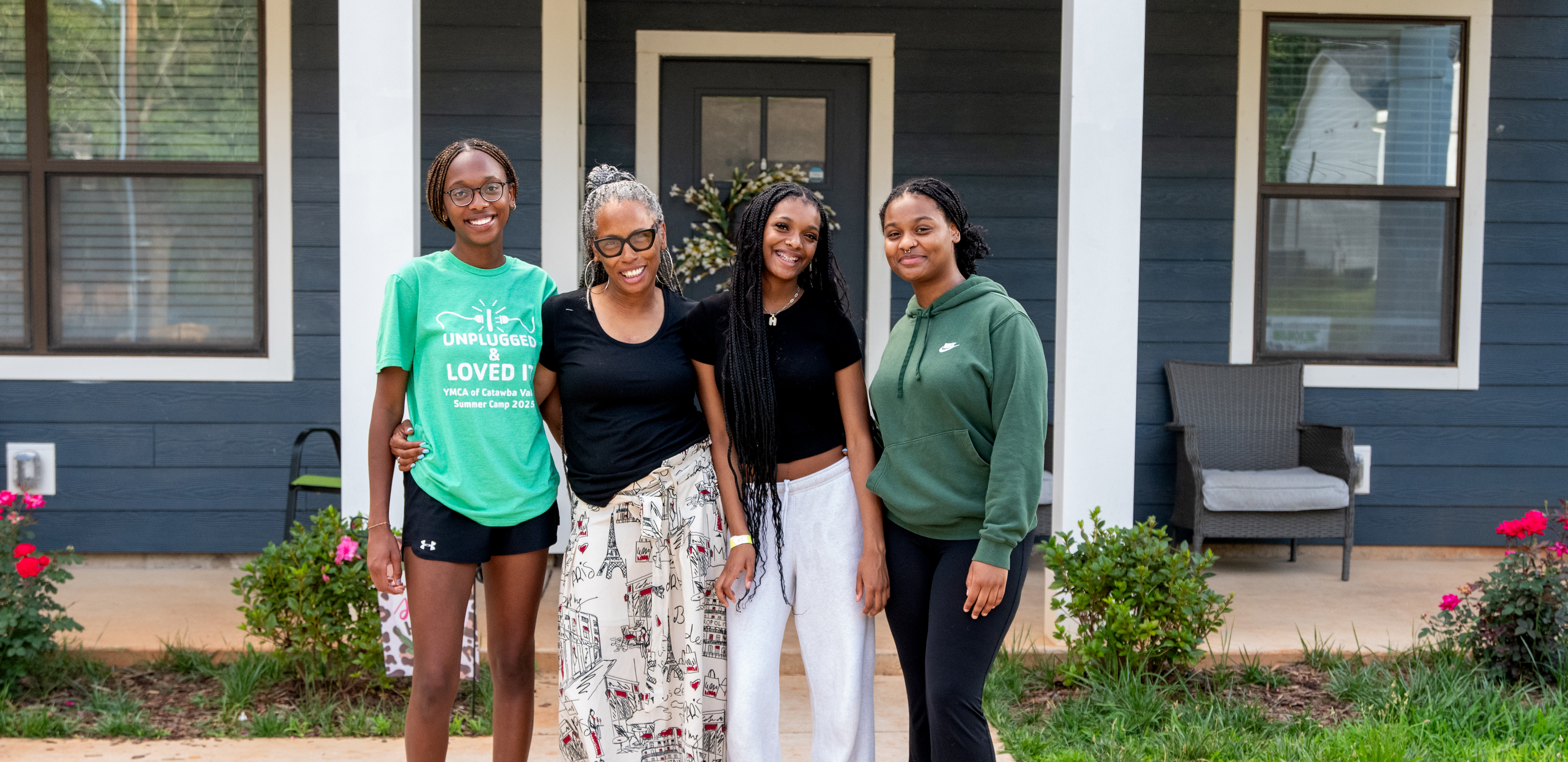 Three teenage girls and their grandmother posing in front of their home.