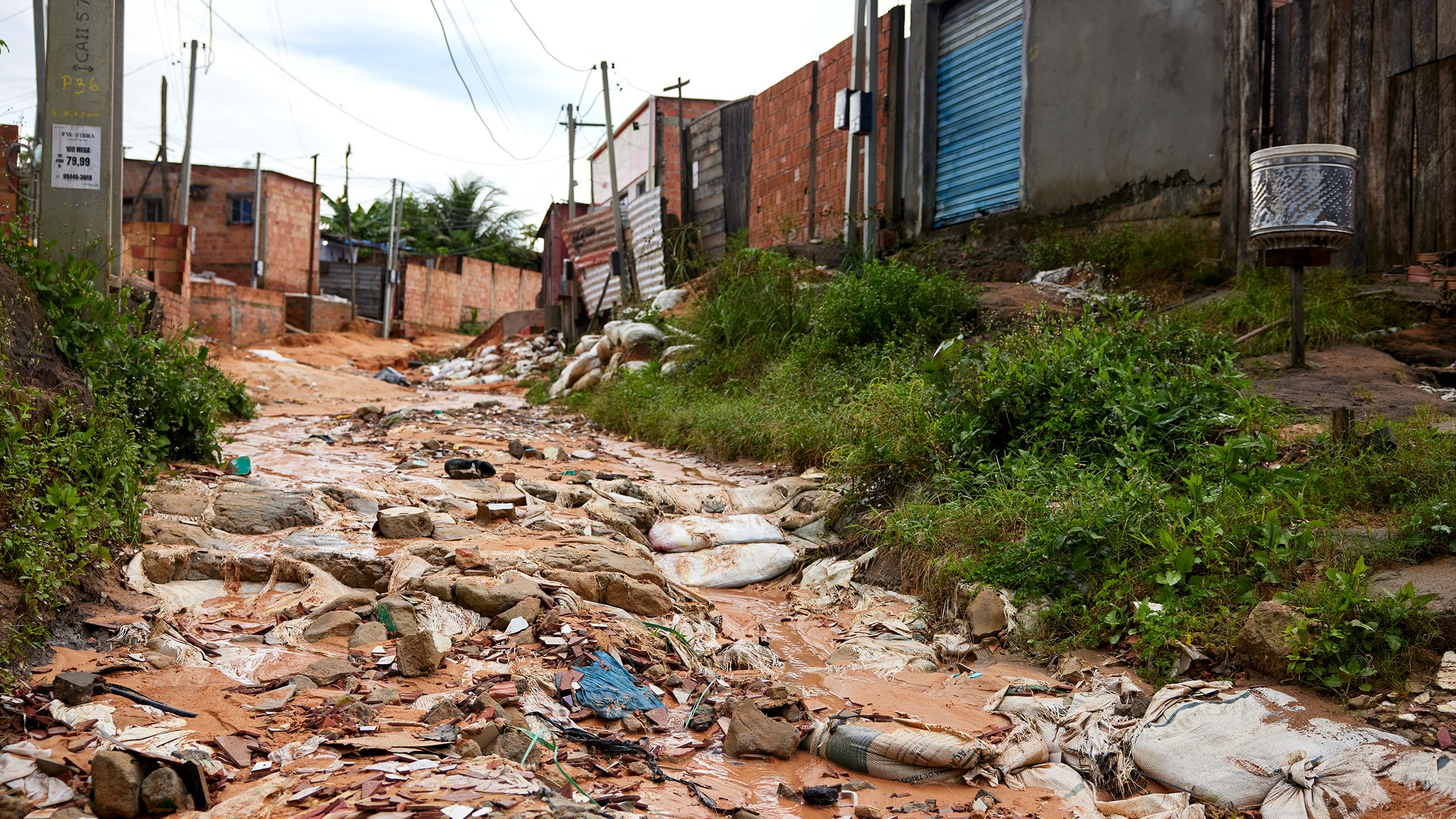 A muddy, deeply rutted roadway is thickly strewn with loose trash, rocks and debris.