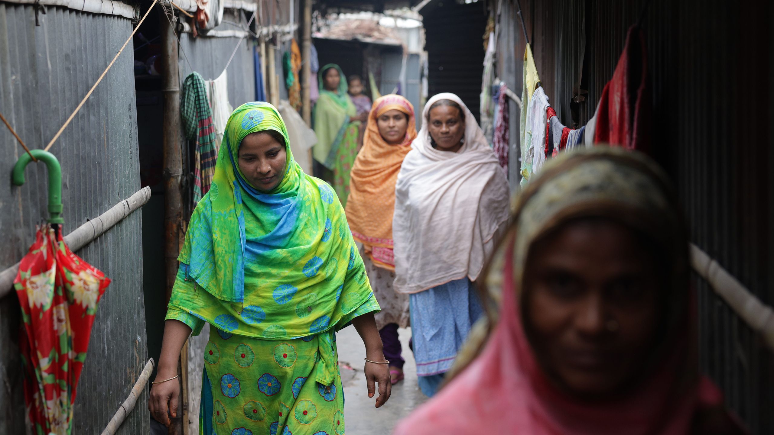 Seen from the front, Sahana (in a green sari) leads a group of her neighbors down a narrow pathway.