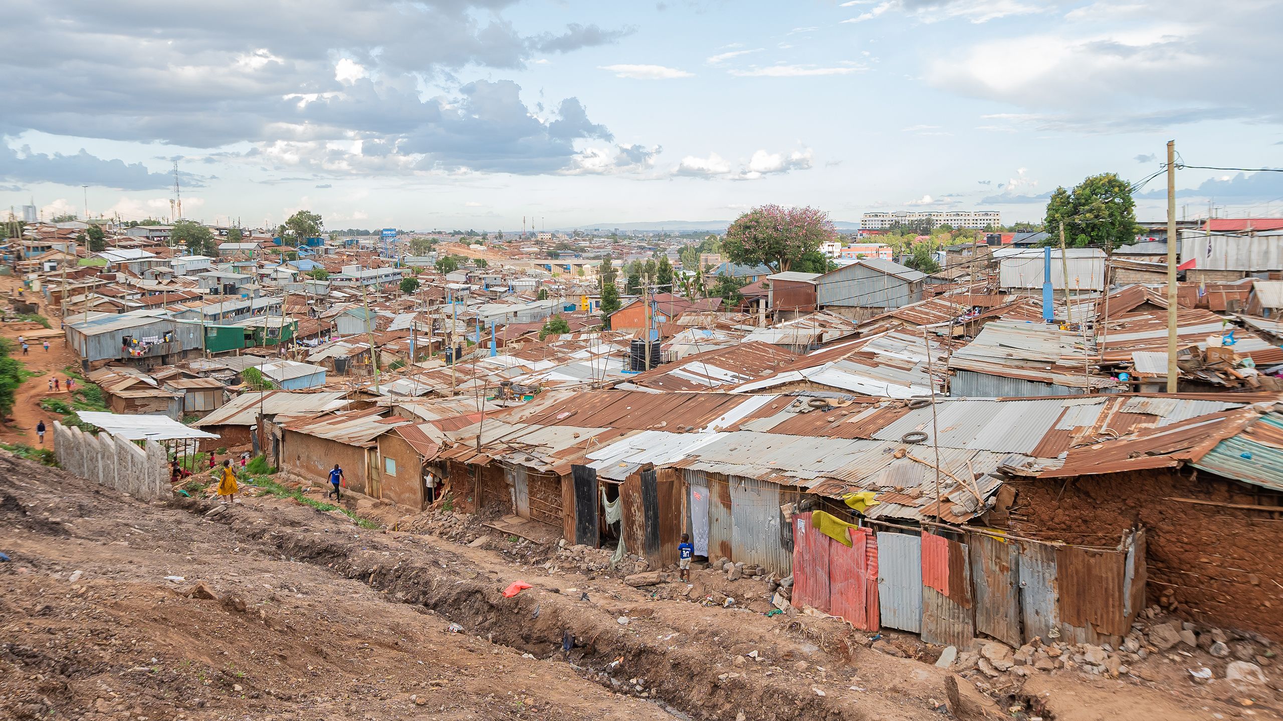 Small homes build of rusting corrugated metal and crumbling clay brick are densely packed in an informal settlement.