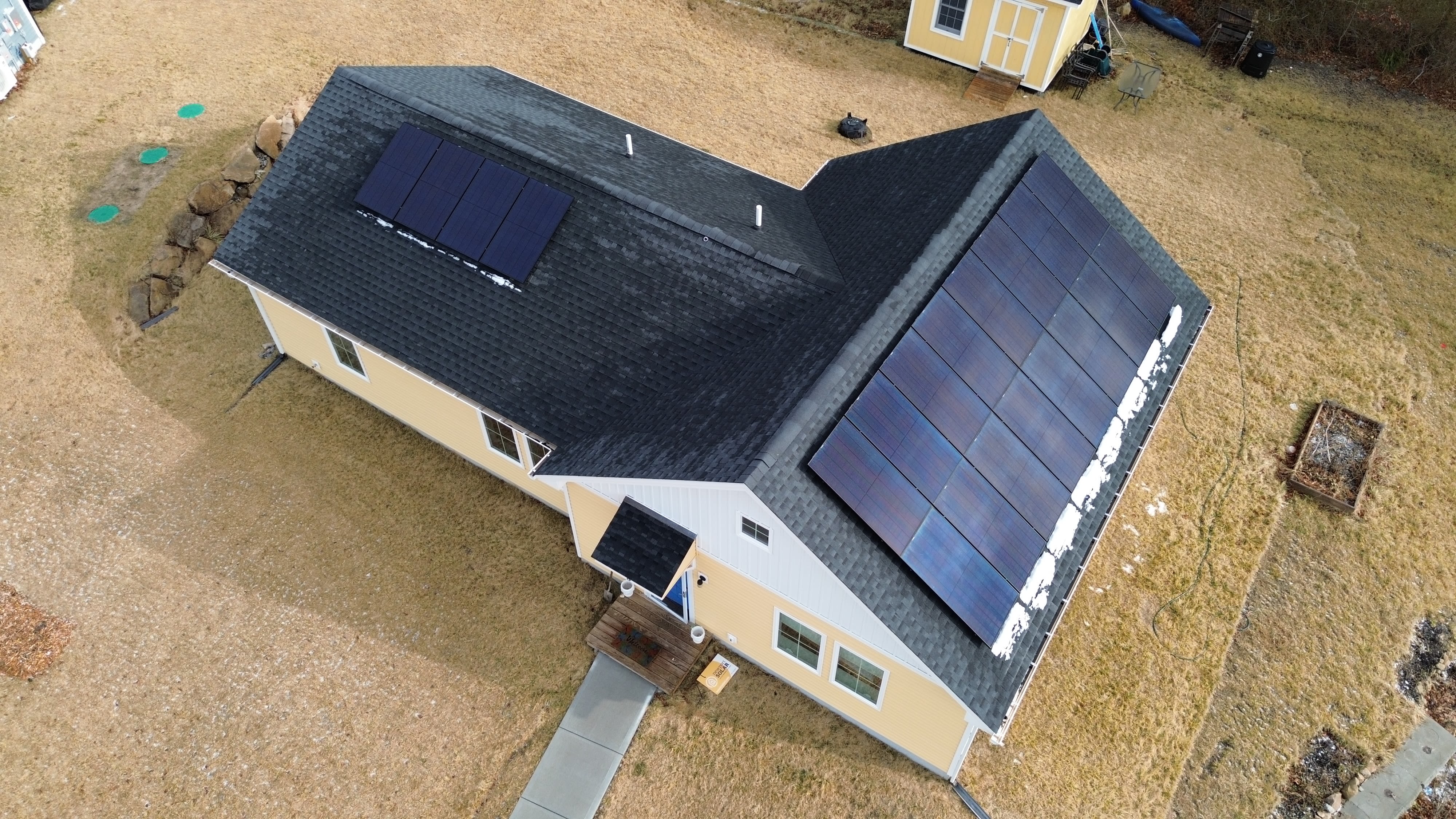 Aerial view of a yellow house with solar panels on the rooftop.