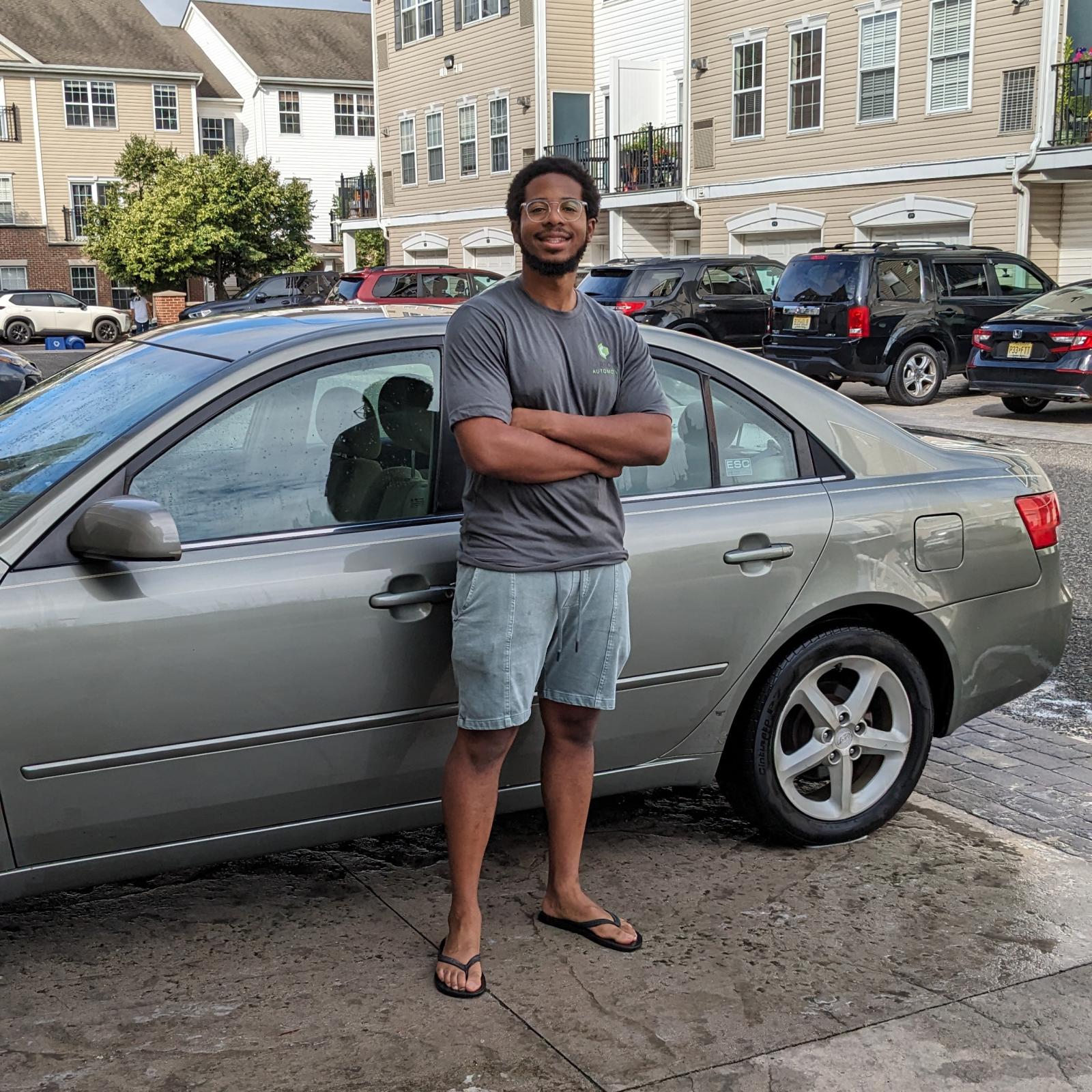 Gray Hyundai Sonata with a man in shorts and a gray shirt standing in front of it.