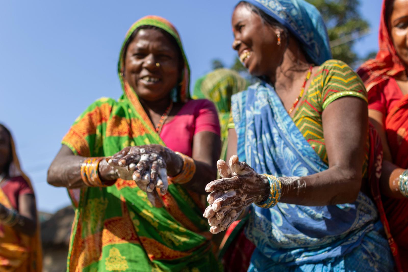 Two women in colorful saris washing their hands.