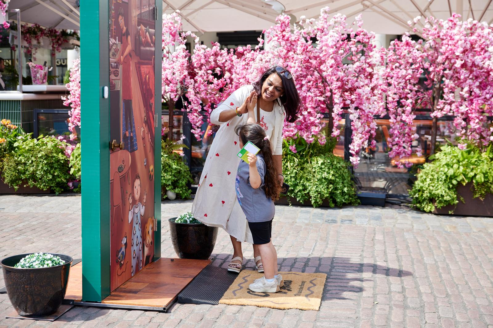 A mother and young daughter viewing an illustrated door in front of cherry blossoms.