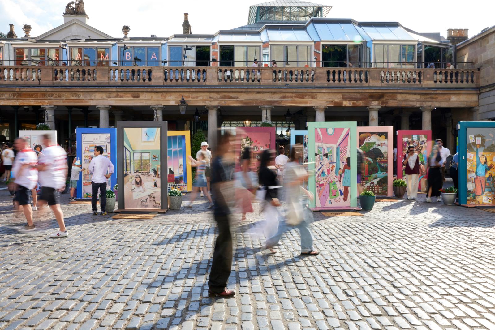 The pop-up door exhibit sits in the background. People are blurred in the foreground as they walk by.