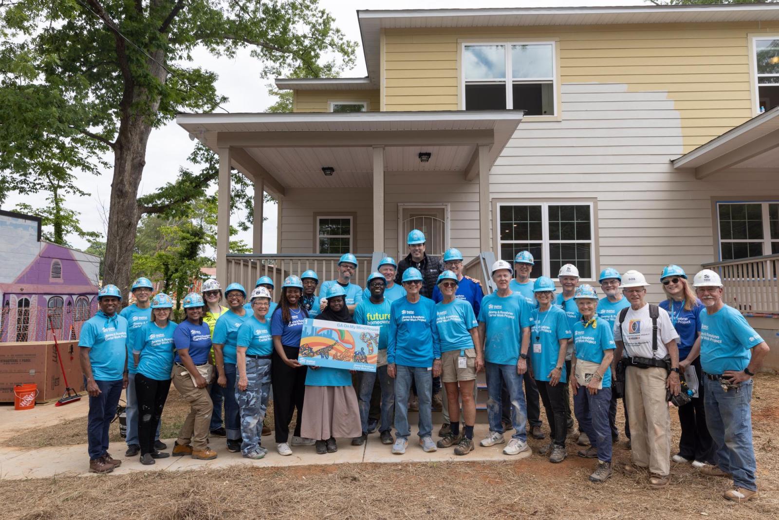 House 1 volunteers stand in front of a partially painted home.