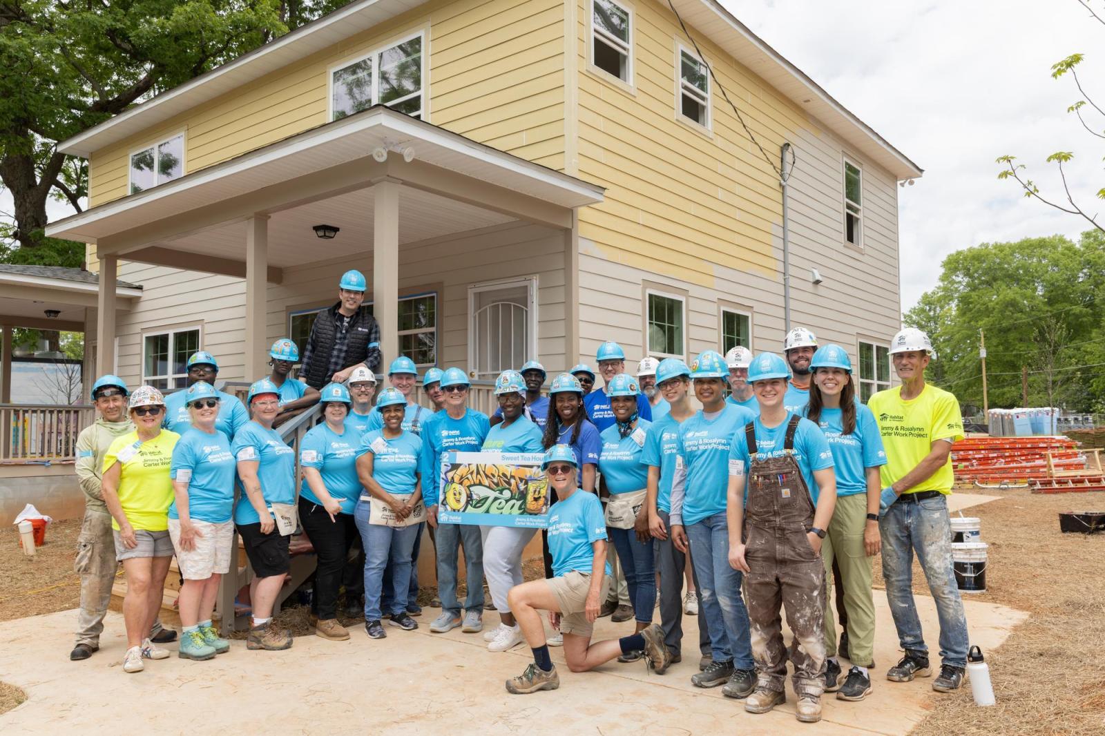 House 2 volunteers posing in front of partially-painted house.