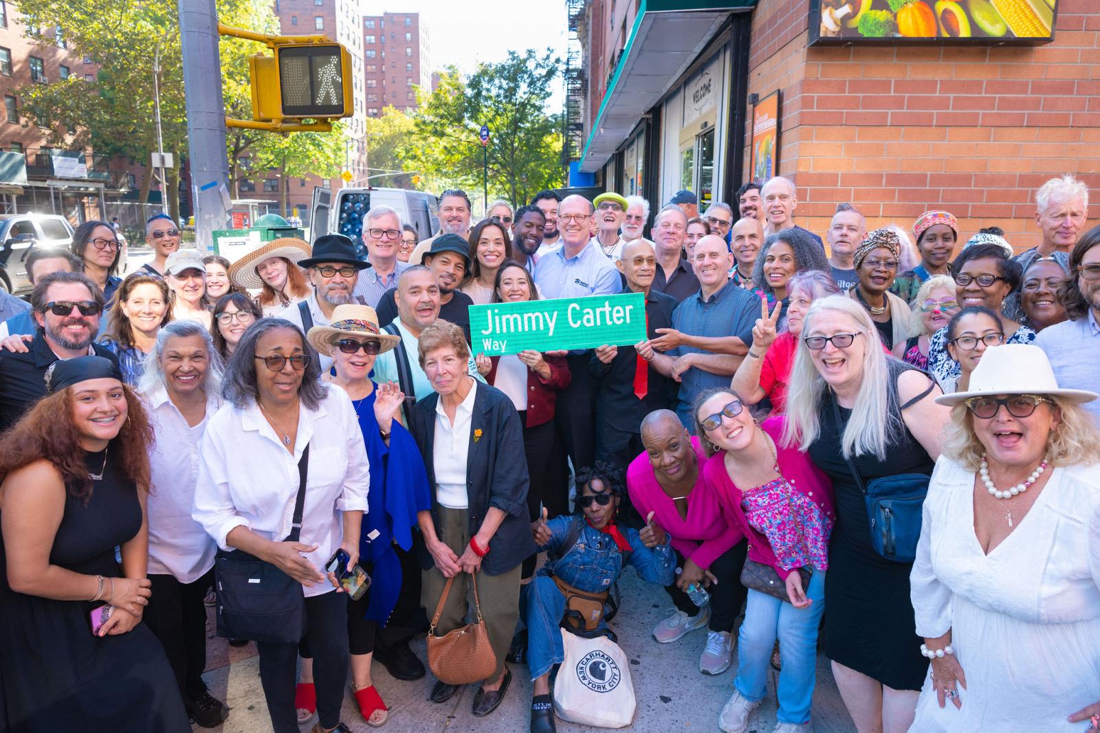 Large group of smiling people gathered around a street sign reading "Jimmy Carter Way."