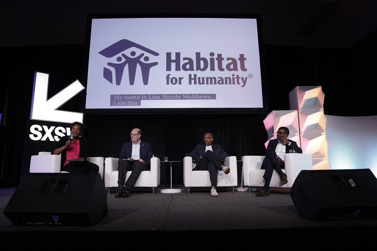 Participants in a panel discussion at SXSW sitting on a stage under the Habitat for Humanity logo.