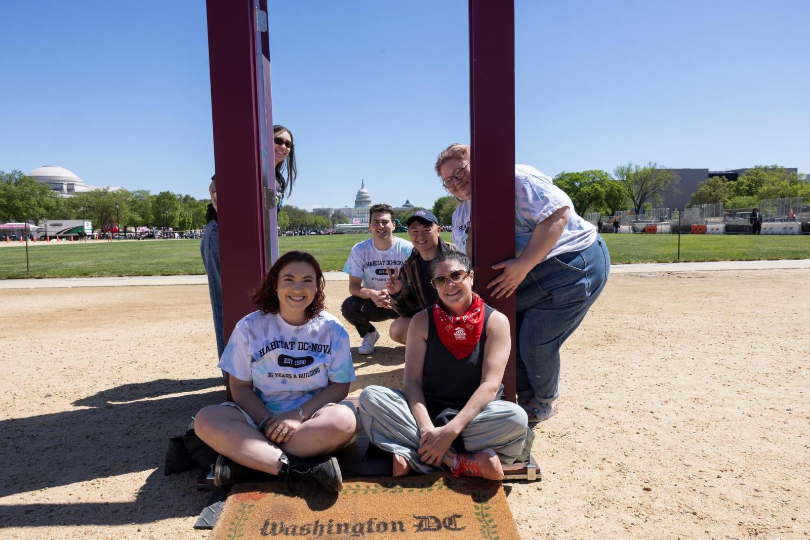 Group of five people sitting on the ground of kneeling near a purple door frame.