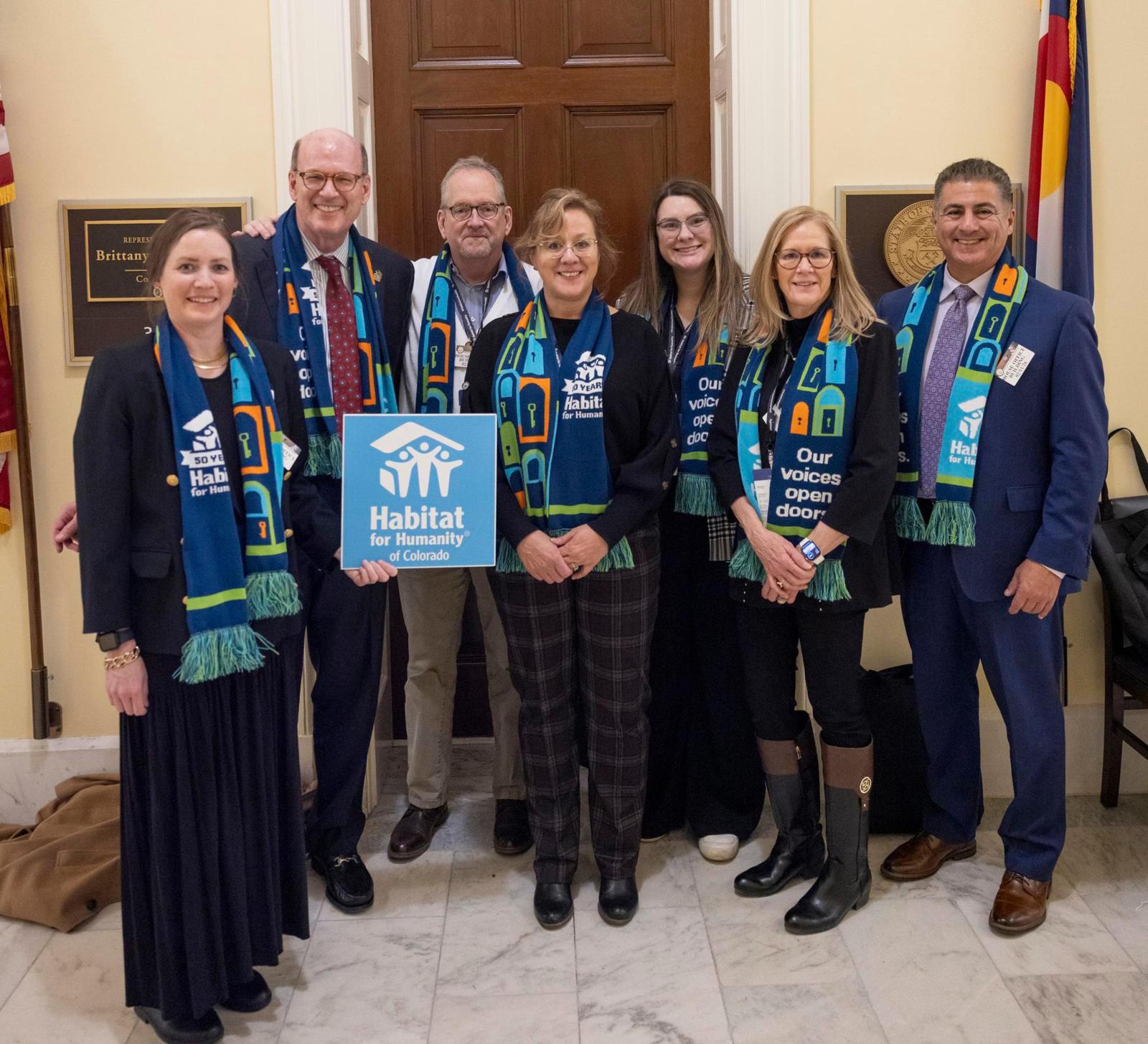 Group of people wearing Habitat on the Hill scarves posing with a Habitat sign.