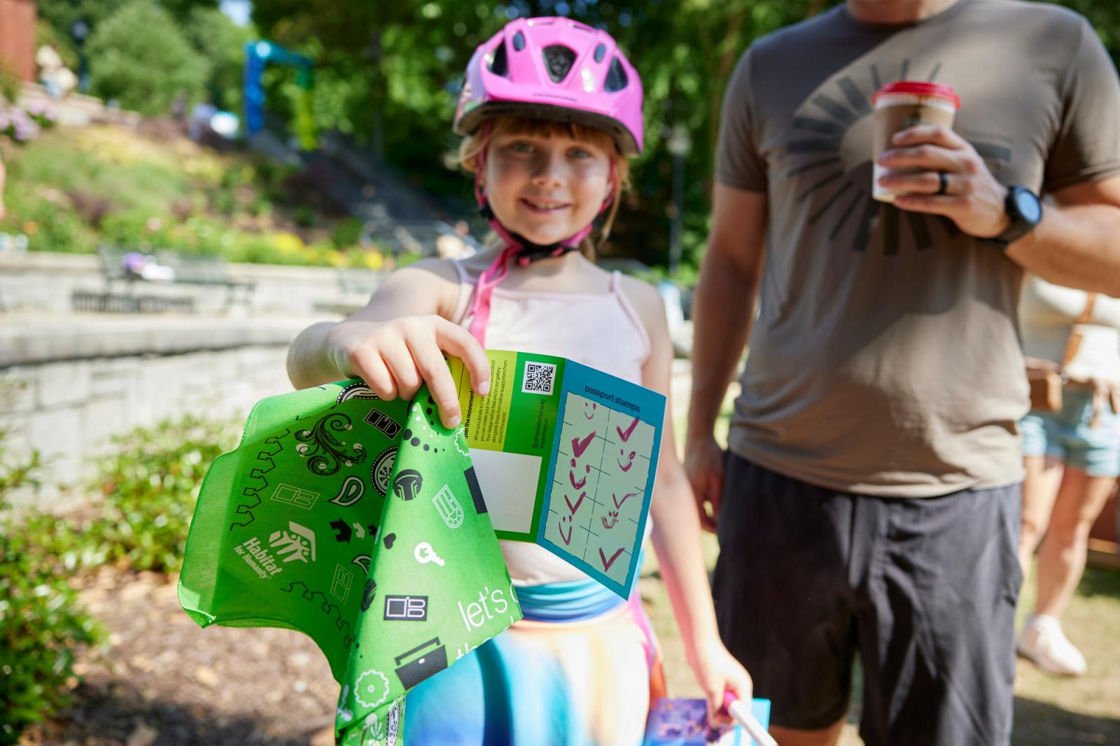 Child in a pink helmet holding up her door passport and green bandana.