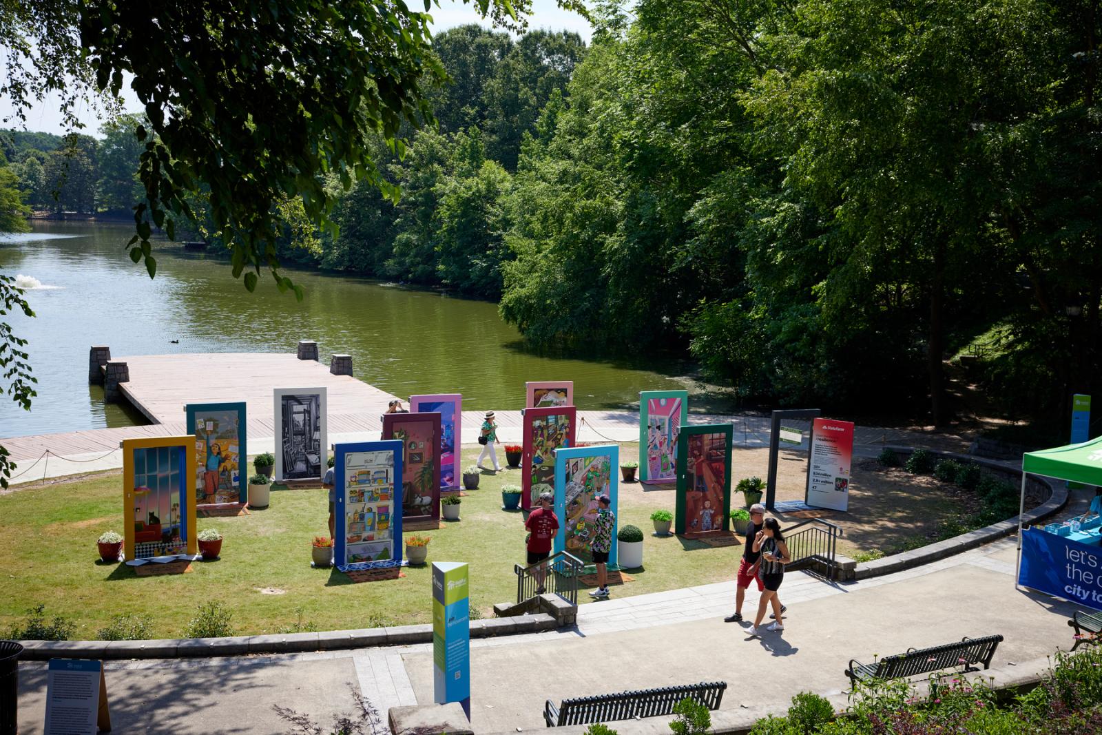 A wide lens shot of the door exhibition. Ten decorated doors and doorframes stand on a grassy area with a lake behind it.