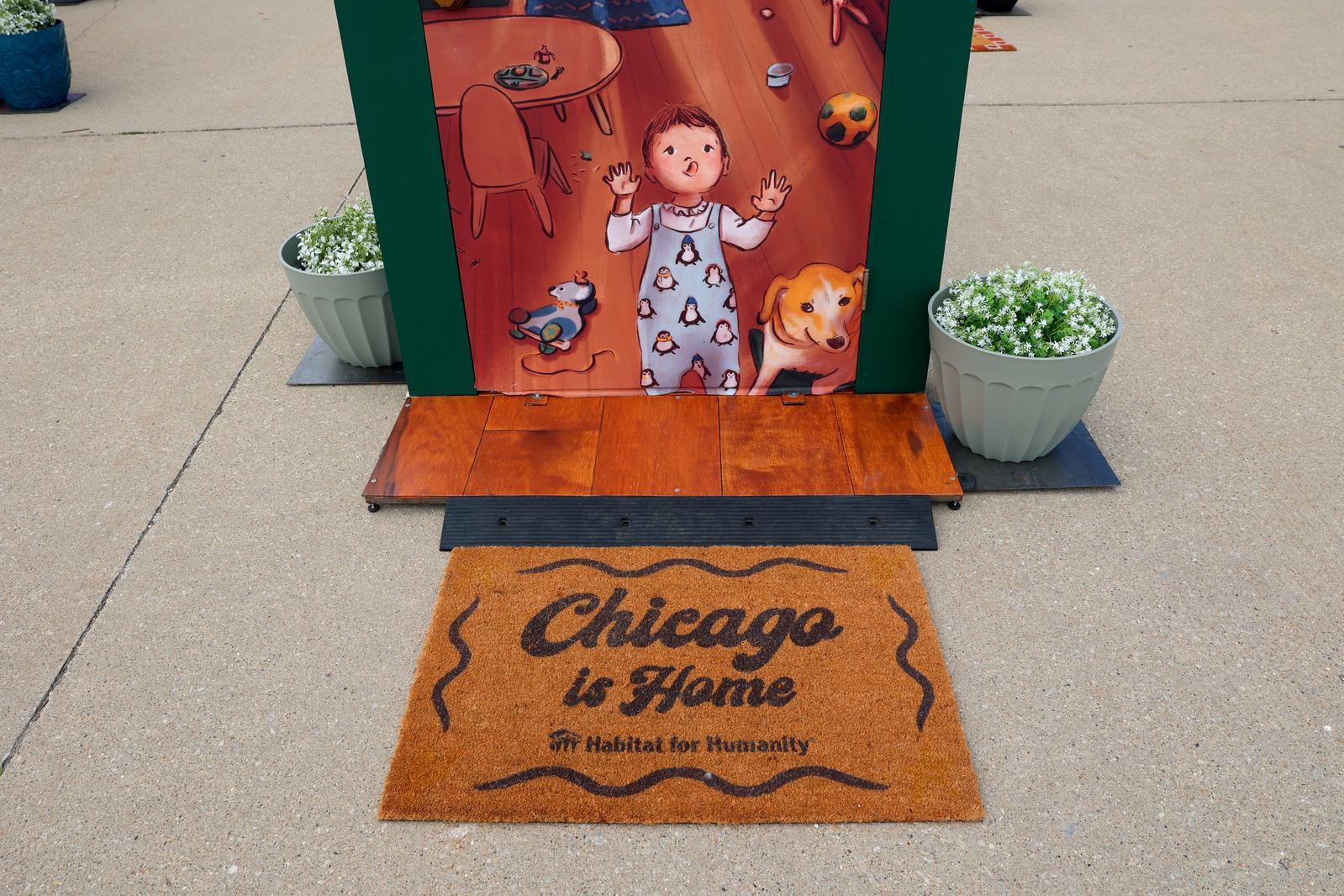 Door mat that says, "Chicago is home" in front of an illustrated door with a toddler and his toys.