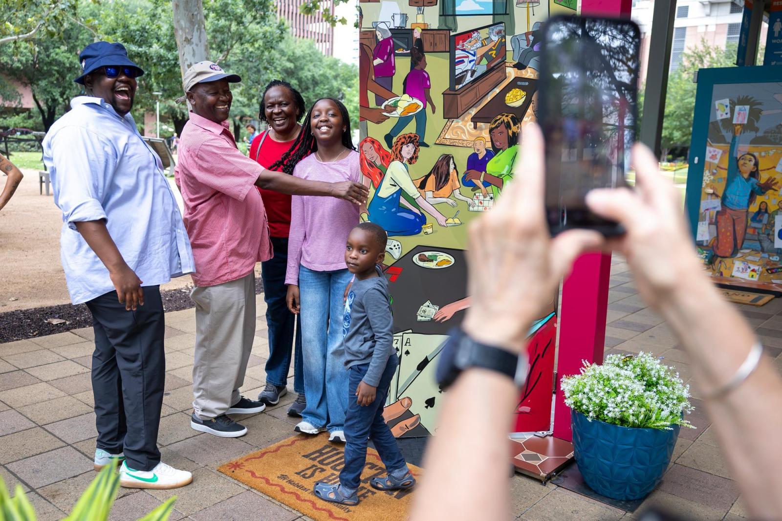 Family, including a small boy, posing in front of a door while someone takes a photo on a cell phone out of frame.