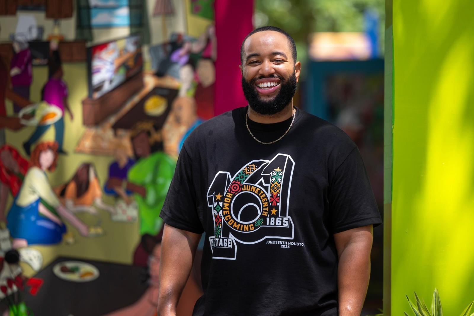 Man in black t-shirt with a beard posing in front of the door he designed. 