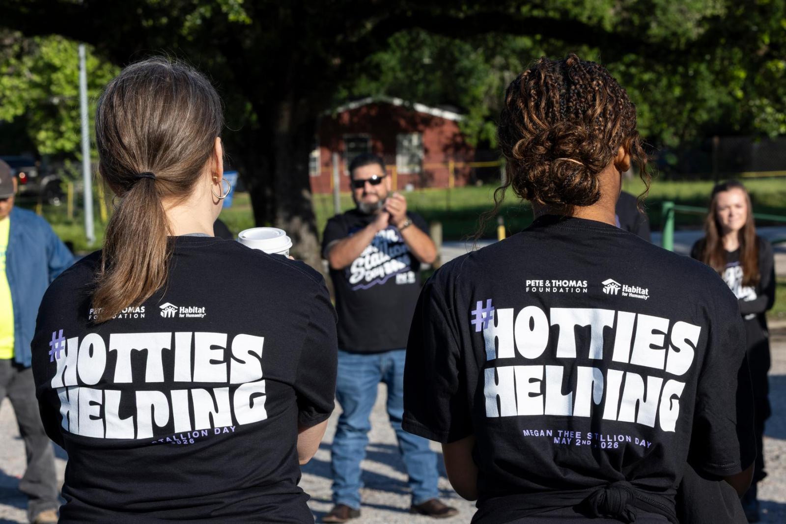 Two volunteers wearing black shirts with their back to the camera. The shirts say Hotties Helping in white letters. 