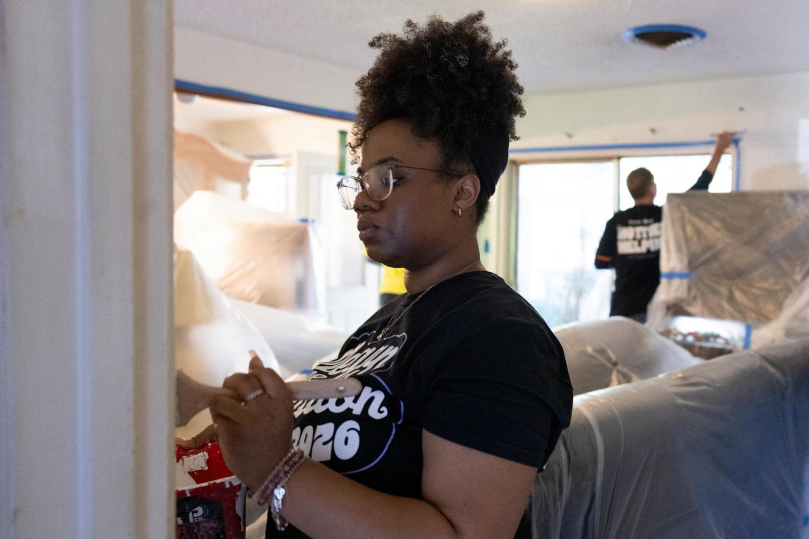 A volunteer in a black t-shirt focuses in on the detail of a doorframe and paints it white.