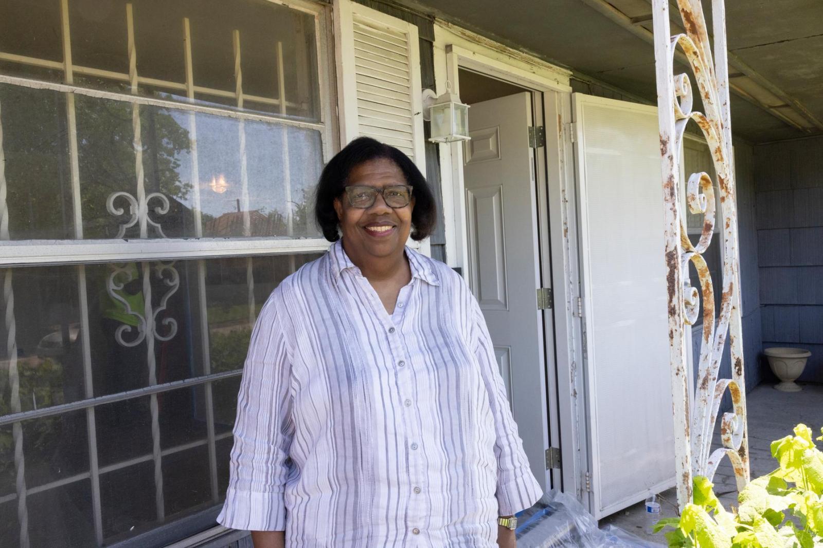 A homeowner in a striped button-down t-shirt stands outside her home and smiles in front of her home during Megan Thee Stallion Day.