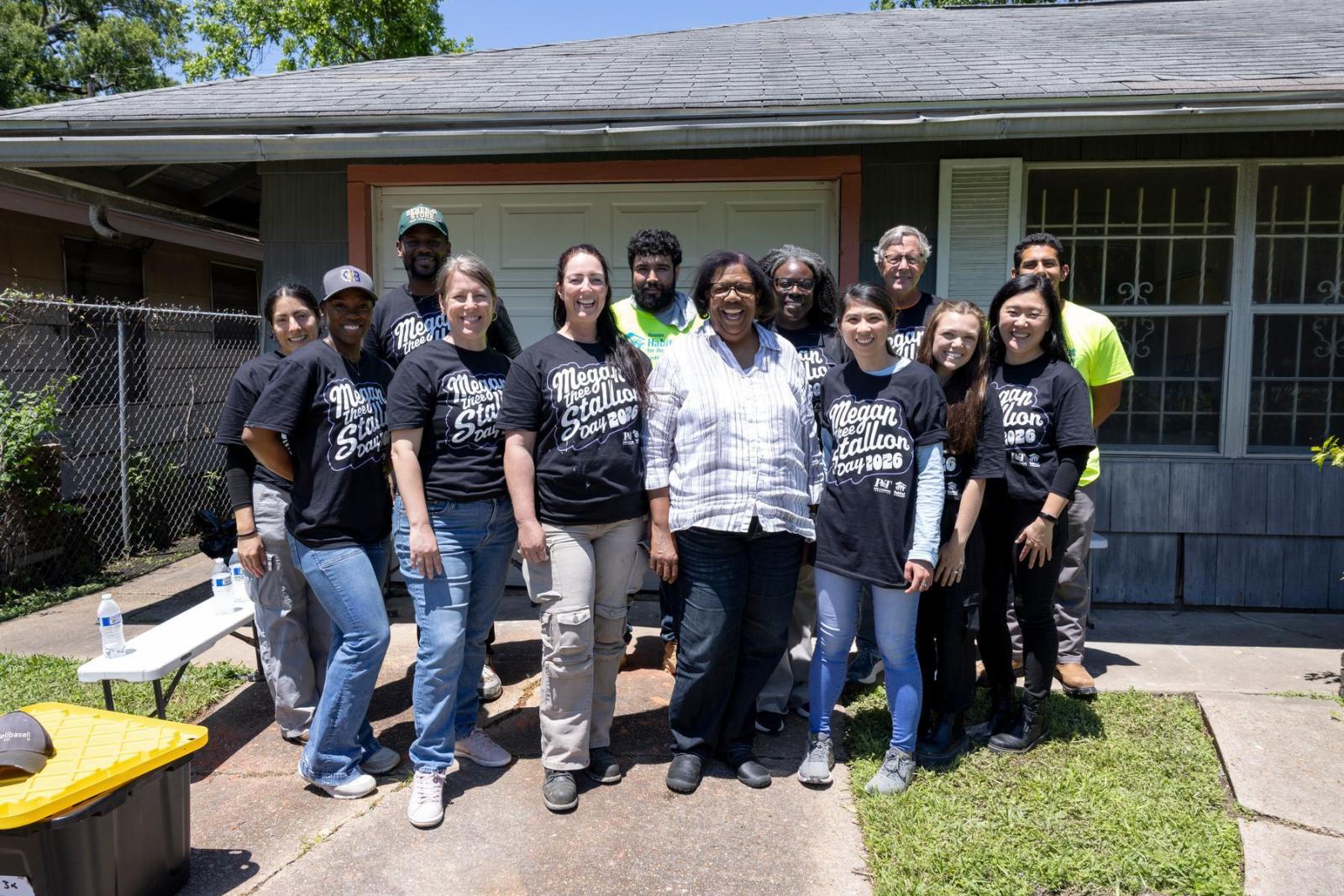 A homeowner stands in the middle of a group of volunteers in front of her home.