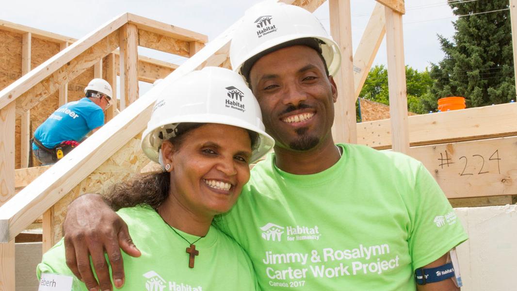 Habitat homeowners Teberh and Alem pose on build site wearing hard hats