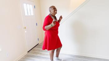 Habitat homeowner in a red dress happily dancing in her new living room