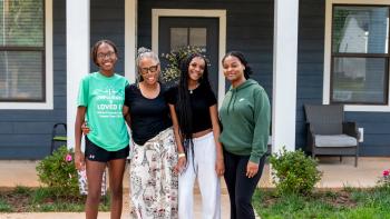 Three teenage girls and their grandmother posing in front of their home.