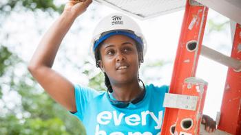 Young woman wearing a hard hat on a ladder.