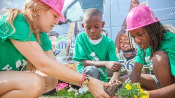A teenage girl, a young boy and another girl are planing flowers.