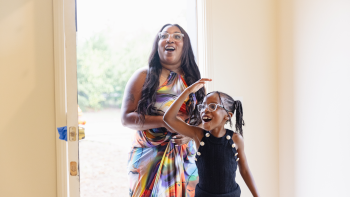 A mother and her young daughter walking through the front door of their new home with a look of delighted surprise and excitement on their faces.