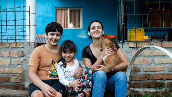 Woman sitting in front of her blue house with her two children and dog.