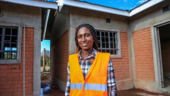 A woman wearing a construction vest stands before a construction site