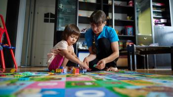 A mom sits on a rug playing games with her daughter.