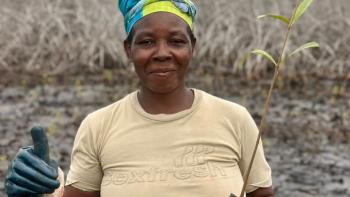 A woman holds a mangrove seedling and a thumbs up