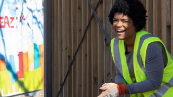 Woman in a bright yellow vest cleaning up her neighborhood smiles to someone off camera.