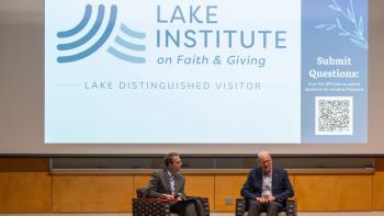 Jonathan Reckford seated on stage with an interviewer in front of a projector screen showing event information, including "Lake Institute on Faith & Giving" and "Lake Distinguished Visitor" 