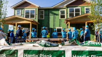 Volunteers stand outside a partially-built house listening to safety information before beginning work.