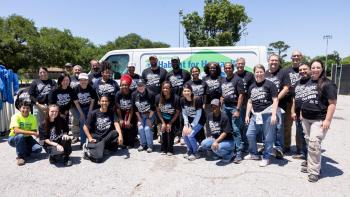 A group of volunteers wearing black t-shirts that say Megan Thee Stallion Day pose in front of a white van in a big group and smile for the camera.
