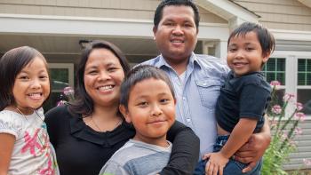 Two parents outside their home holding their three children, smiling.