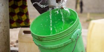 A woman fills up a green bucket with water from a water kiosk.