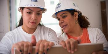 Two people wearing hard hats while working on a house.