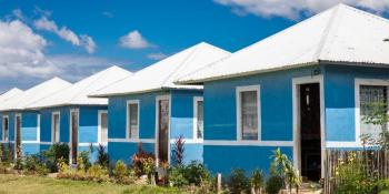 Row of bright blue Habitat houses with white roofs in front of a clear blue sky with fluffy white clouds.