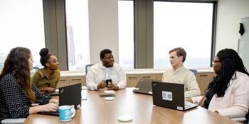 A group of young professionals sitting at a table together with laptops, holding a meeting in the Habitat headquarters office.