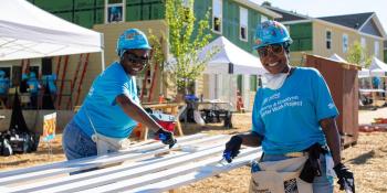 Volunteers painting trim on the site of the Carter Work Project. Behind them, the houses are in various states of completion.