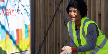 Woman in a bright yellow vest cleaning up her neighborhood smiles to someone off camera.